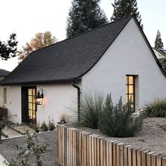 a white house with a black roof and wooden fence in front of the house is surrounded by greenery