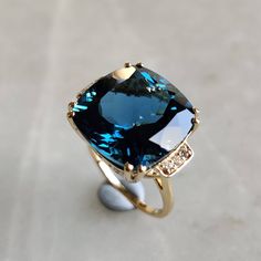 This stunning ring is set in 14k Solid Yellow Gold with Natural London Blue Topaz and Diamond with utmost precision. It is an unique statement gemstone ring for nearly every occasion and is completely hassle-free jewelry. ITEM DETAILS * CENTER GEM: London Blue topaz * GEM SIZE: 15X15mm * GEM SHAPE: Cushion * Gem weight: 15.95 carats * SIDE GEM: Diamond * GEM SIZE: 1.50mm (6 pcs),  * GEM SHAPE: ROUND * Gem weight: 0.083 carats * Total Gem weight: 16.03 carats * Gold Purity: 14KT * Gold Weight: 3.58 gram * Total Weight of the Ring: 6.79 gram The Gold purity is guaranteed and it comes with authentic 14KT gold hallmark. Since my items are handmade, they are absolutely nickel and lead free. CUSTOMIZATION: * Size Customization is available for this ring and it is available in all ring sizes. Kin Luxury Gold Topaz Ring With Gemstone Accents, Blue Gem Rings, Luxury Timeless Gold Topaz Ring, Classic Luxury Topaz Ring With Polished Finish, Luxury Vintage Topaz Ring As A Gift, Yellow Topaz Ring Designs, Modern Blue Topaz Ring In 14k Gold, Blue Cushion Cut Ring With Gemstone Accents, Elegant Blue Topaz Ring In 14k Gold