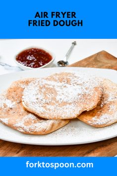 a white plate topped with pancakes covered in powdered sugar next to a bowl of ketchup