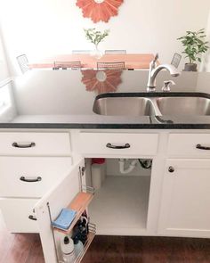 An open cabinet door exposes the many ways you can utilize storage in your kitchen with shelves mounted inside the cabinet. The rest of the cabinets form the base of a kitchen island, complete with a black countertop. Over the island, you can see a small dining table surrounded by netted chairs...   Image: growingminimalist