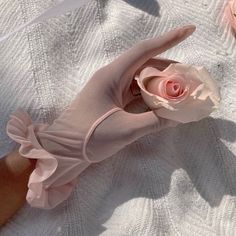 a woman's hand holding a pink flower on top of a white sheet covered ground