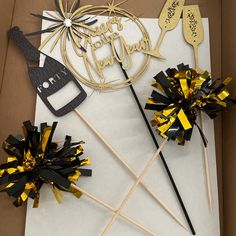 two black and gold cake toppers on sticks in a box with some tags attached to them