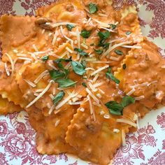 a red and white plate topped with ravioli covered in sauce, cheese and herbs