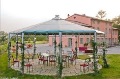 an outdoor dining area with tables and chairs under a gazebo in front of a pink house