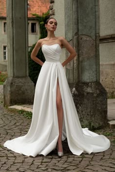 a woman in a white wedding dress standing on a cobblestone street with her legs crossed