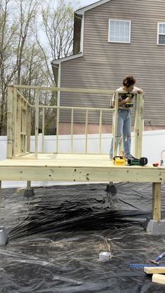 a woman standing on top of a wooden platform in front of a house under construction