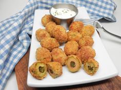 a white plate topped with fried food next to a bowl of ranch dressing and a fork