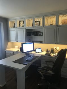 a desk with a laptop and monitor on it in front of some cupboards that have glass doors