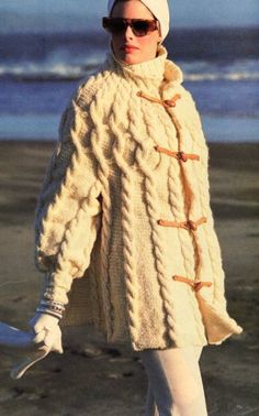 a woman walking on the beach wearing a white sweater and hat with an oversized cabled design