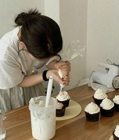 a woman is decorating cupcakes with icing on the table in front of her