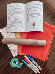 an open book sitting on top of a wooden table next to markers, scissors and tape