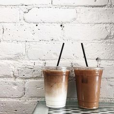 two drinks sitting on top of a table next to each other in front of a white brick wall