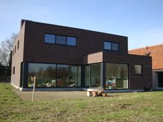 a house with large windows sitting on top of a grass covered field next to a building