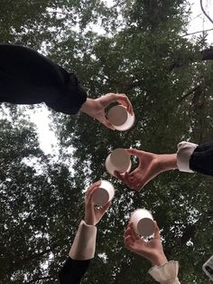 four people holding white cups and saucers in their hands, with trees in the background