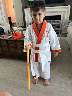 a young boy holding a yellow stick and wearing a white kimono with an orange sash