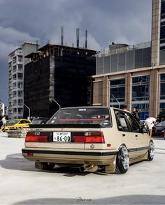 a tan car parked in front of a tall building with people standing around and looking at it