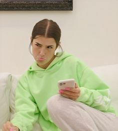 a woman sitting on a couch holding a cell phone and looking at her earphones