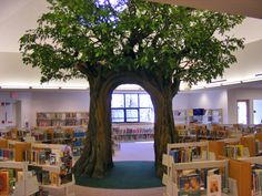 a library filled with lots of books next to a tree in the middle of it