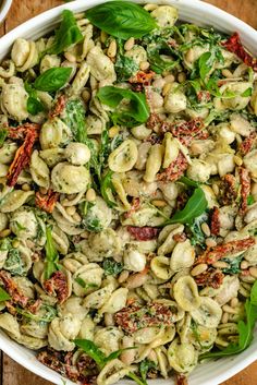 a white bowl filled with pasta and spinach salad on top of a wooden table