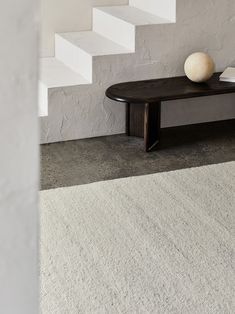 a wooden table sitting on top of a white rug next to a stair case in a room