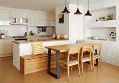 an open kitchen and dining area with white brick walls, wood flooring and modern lighting fixtures