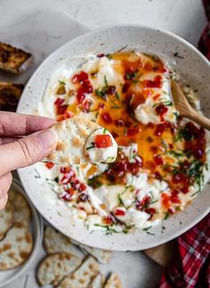 a hand holding a cracker over a bowl of dip with crackers on the side