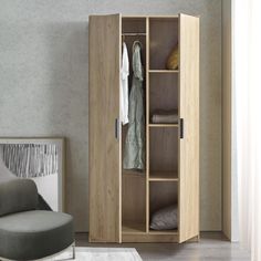 an open wardrobe with clothes hanging on the door and a grey chair in front of it