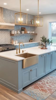 Light blue and white cottagecore kitchen with a vintage island, farmhouse sink, herringbone backsplash, and warm lighting. Marble Herringbone Backsplash Kitchen, Blue Theme Kitchen, Kitchen Blue Countertops, Light Blue And Gold Kitchen, Blue Kitchen White Countertops, Must Haves In Kitchen Remodel, Grandmillenial Style Kitchens, Homes With Color, Blue Kitchen Cabinets White Countertops