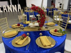 a blue table cloth with gold plates and napkins on it is set for a formal dinner