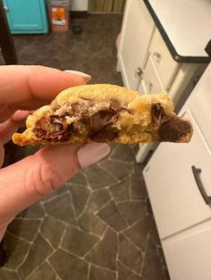 a person holding a half eaten chocolate chip cookie in their hand on the kitchen floor