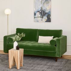 a living room with a green velvet couch and side table in front of a painting