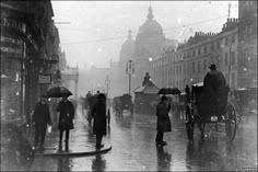 an old black and white photo of people walking in the rain with their umbrellas open