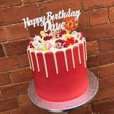 a red birthday cake with white icing and candy on top is sitting in front of a brick wall