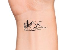 a small tattoo on the wrist of a woman with mountains and trees in the background