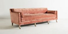 an old pink velvet couch with gold legs and foot rests on a white floor in front of a plain wall