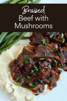 braised beef with mushrooms and mashed potatoes on a white plate next to green beans