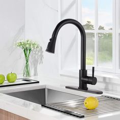 a kitchen sink with a black faucet and some green apples on the counter