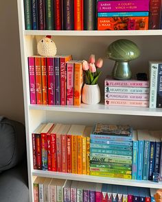 a bookshelf filled with lots of different colored books and vases on top of them