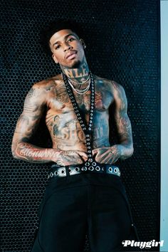 a man with tattoos standing in front of a black wall and holding his hands on his hips