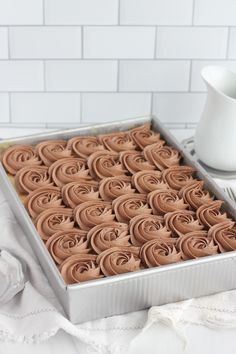 a pan filled with chocolate frosting on top of a white table next to a cup