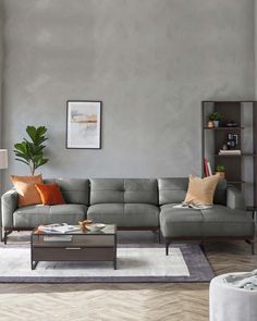 Modern living room setup featuring a grey L-shaped sectional sofa with plush cushions and a sleek dark wooden frame. In front of the sofa is a rectangular wooden coffee table with a dark finish, holding decorative items and books. To the right, a dark wood bookshelf is adorned with a variety of decorative objects and plants, contributing to a contemporary aesthetic. Grey Sofa Inspiration, Grey Leather Sofa Living Room, Grey Leather Corner Sofa, Headrest Sofa, L Shaped Leather Sofa, Living Aesthetic, Grey Leather Sofa, Comfortable Living Room, Living Room Aesthetic