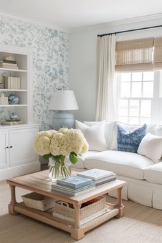 a living room filled with furniture and flowers on top of a coffee table in front of a window