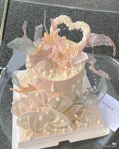 a three tiered wedding cake with pearls and flowers on display in a glass case