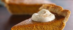 a slice of pumpkin pie with whipped cream on top, sitting on a wooden table