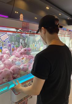 a man standing in front of a vending machine filled with pink teddy bears and other stuffed animals