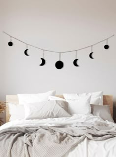 a bed with white sheets and four phases of the moon hanging above it