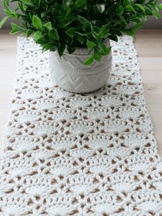 a crocheted table runner with a potted plant in it on a wooden surface