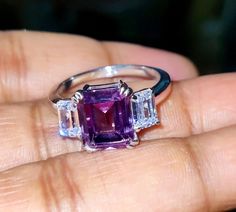 a woman's hand holding an amethoraite and diamond three stone ring