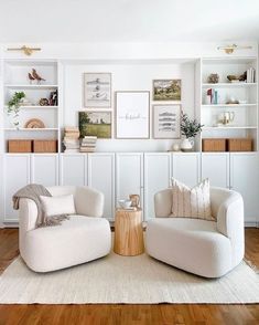 two white chairs sitting on top of a hard wood floor next to bookshelves