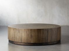 a round wooden table sitting on top of a cement floor next to a white wall